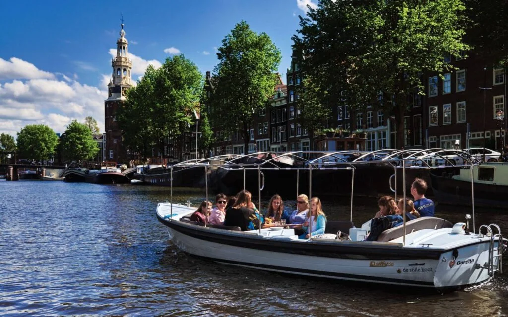 Boat tour guests enjoying sunny day on Oudeschans canal, historic Montelbaanstoren in background