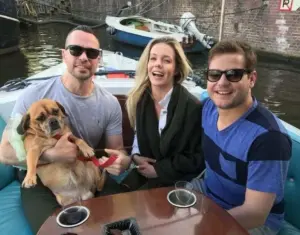 Dog lying belly up on the lap of its favorite owner while three friends laugh together on a dog friendly canal cruise through Amsterdam