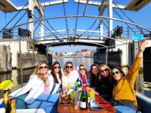 Group of ladies enjoying a canal cruise through central Amsterdam with wine while sailing underneath the skinny bridge on a sunny day.