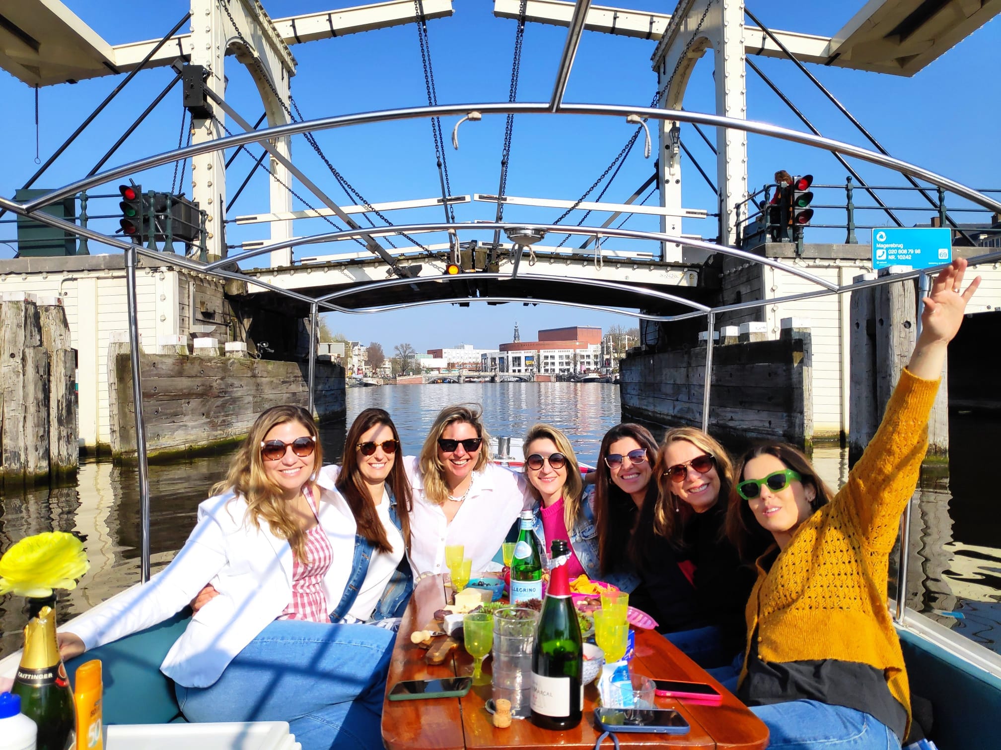 Group of ladies enjoying a canal cruise through central Amsterdam with wine while sailing underneath the skinny bridge on a sunny day.